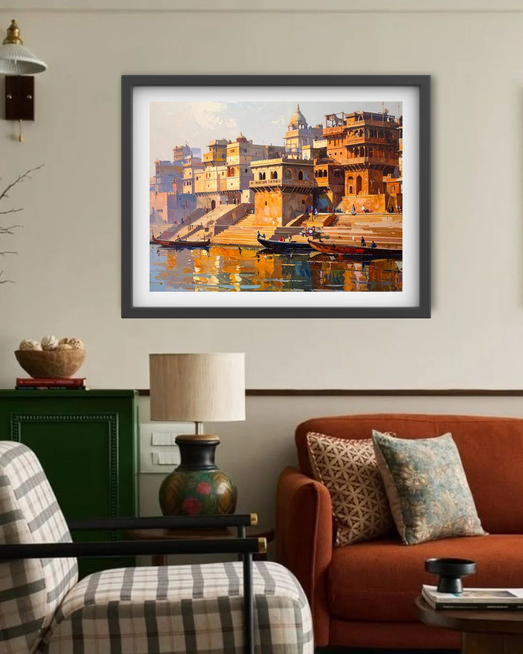 A framed art print depicting a warm-toned painting of a riverfront city with boats and buildings, displayed on a beige wall above a living room setup with an orange sofa, lamp, and chair.