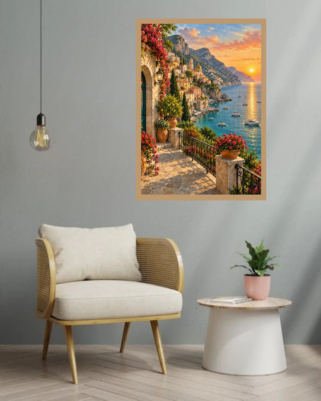 A framed art print depicting a scenic coastal village with a sunset over the sea, hung on a gray wall above a modern armchair and side table.