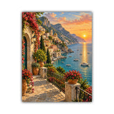 A vertical canvas print depicting a scenic coastal town with a stone walkway, vibrant red flowers, and a sunset over a blue sea with boats, shown against a plain white background.