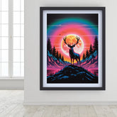 A framed art print featuring a stylized deer silhouette standing on a hill in front of a large glowing moon, with a rainbow arch over mountains and trees. The print is displayed on a white wall in a bright room with a window and light wood floor.