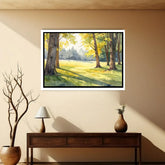 Framed landscape painting of a sunlit forest on a beige wall above a wooden console table.