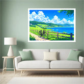 A framed landscape art print depicting a scenic coastal path with a bicycle, green hills, and a blue sky, displayed on a sage green wall above a white sofa in a modern living room setting.