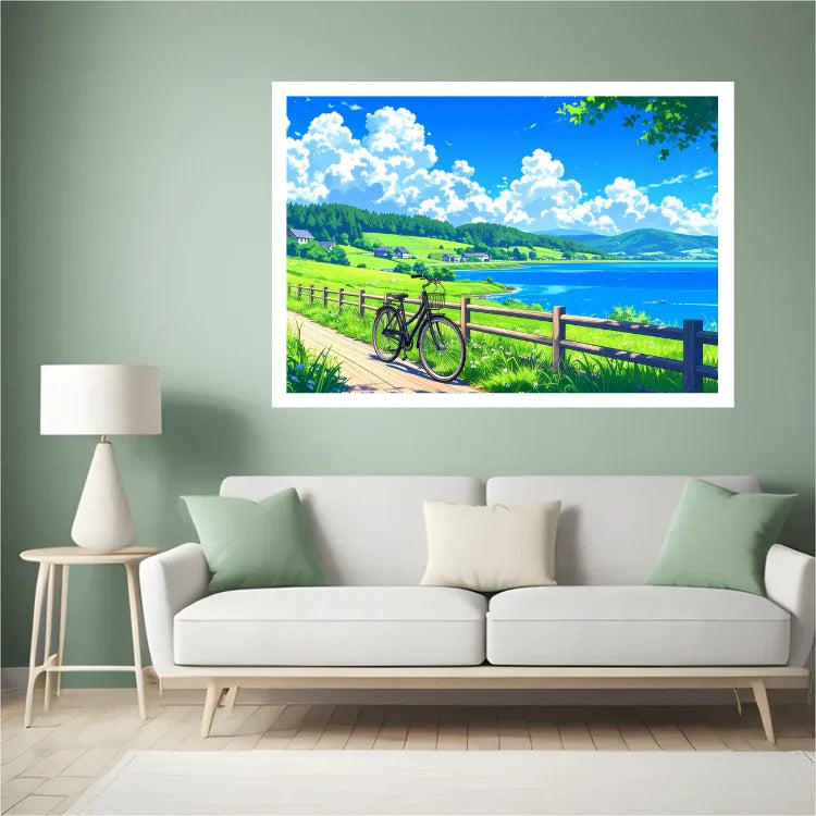 A framed landscape art print depicting a scenic coastal path with a bicycle, green hills, and a blue sky, displayed on a sage green wall above a white sofa in a modern living room setting.