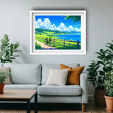 A framed art print depicting a scenic landscape with a blue lake, green hills, and a bicycle on a path, displayed on a light gray wall above a modern light gray sofa with decorative pillows in a living room setting.