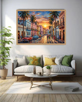 A framed canvas print of a colorful street scene in Havana, featuring palm trees, vintage cars, and a sunset, displayed on a white wall above a modern sofa in a living room setting.