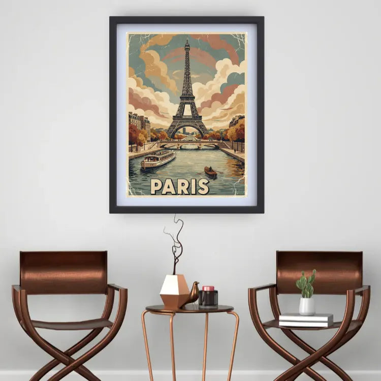 A framed vintage-style Paris travel poster hangs on a light gray wall above a small round side table, with two brown chairs on either side. The poster depicts the Eiffel Tower, boats on a river, and the word PARIS at the bottom.
