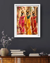 A framed art print depicting three Indian women in colorful traditional saris carrying brass pots, displayed on a dark gray wall above a wooden console table with books and a vase.