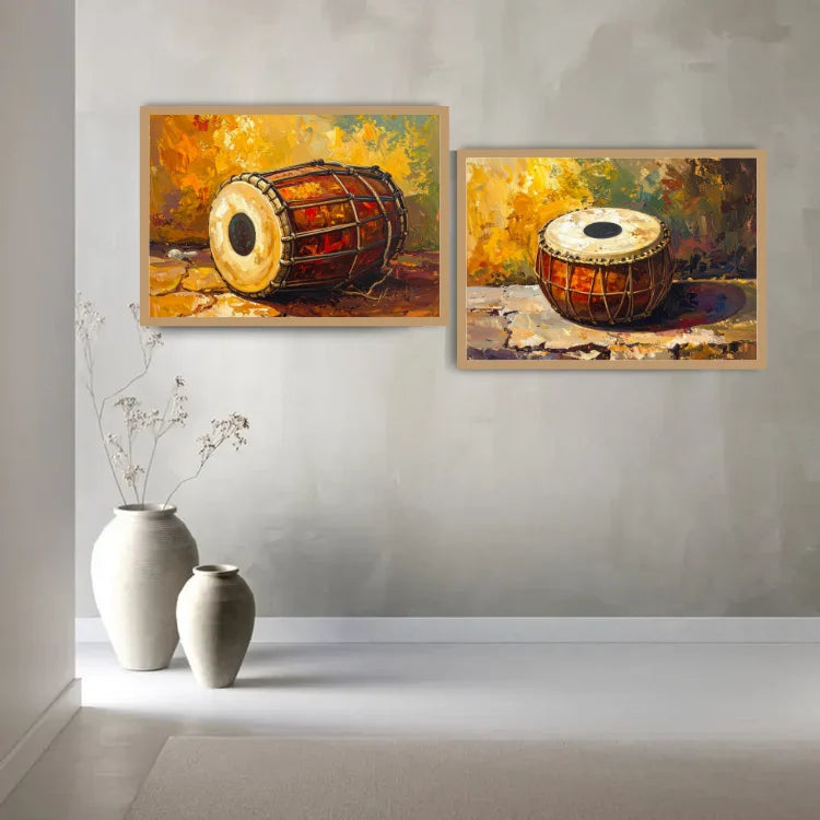 Two framed paintings of traditional drums hanging on a light gray wall above two white ceramic vases.