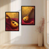 Two framed wall art prints showing traditional stringed instruments in warm golden and red tones, displayed on a white paneled wall above a light wood floor, with a vase of branches to the right.