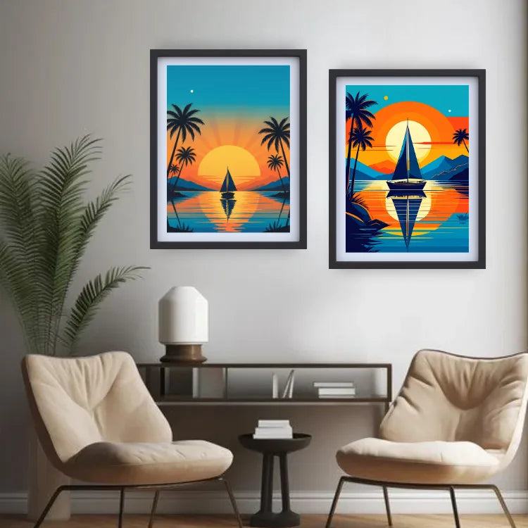 Two framed tropical sunset art prints hang on a light gray wall above a console table with two beige armchairs and a potted plant. The left print shows a sailboat on a lake with palm trees and a large orange sun, and the right print shows a sailboat with mountains, palm trees, and a bright orange sky.