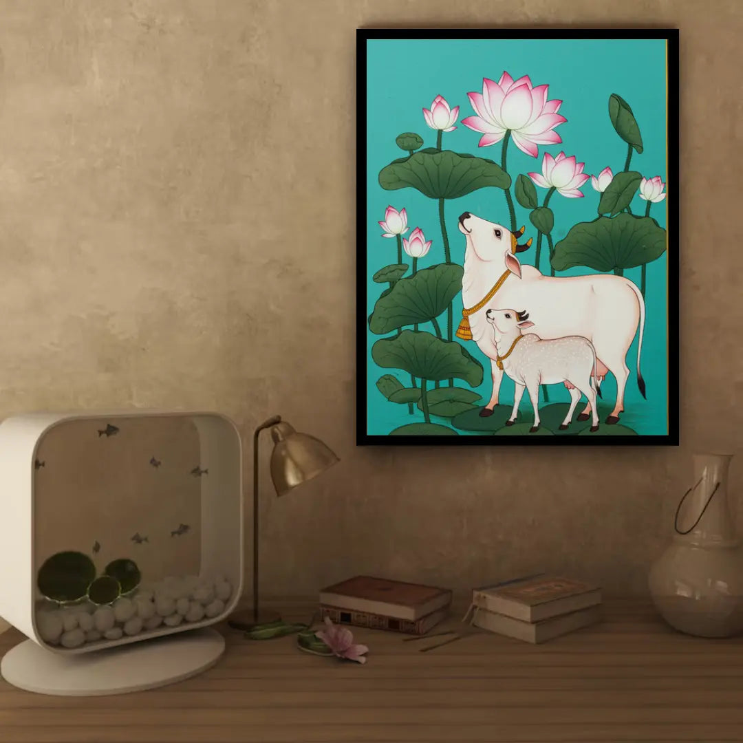 Framed artwork of a cow and calf among lotus flowers on a wall above a wooden surface with decorative items.