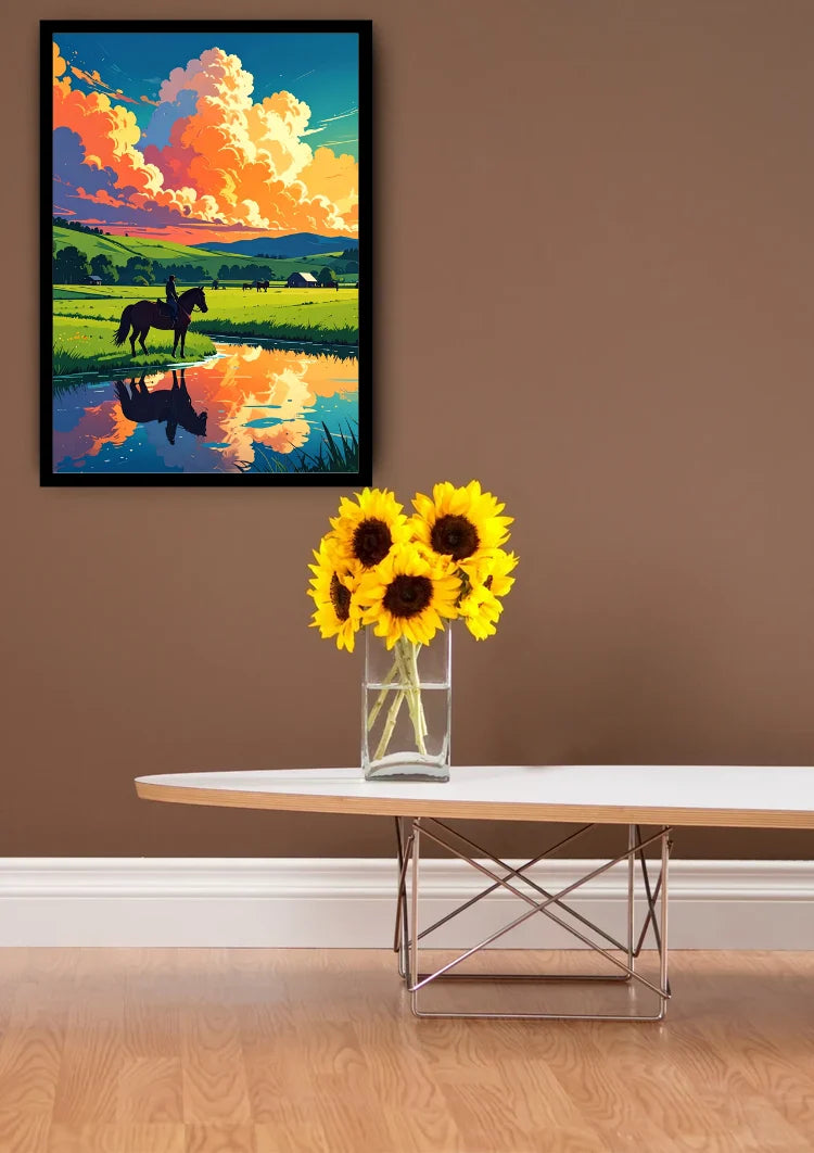 A framed landscape art print depicting a horse in a field under a vibrant sunset sky, displayed on a brown wall above a modern white table with a vase of sunflowers.