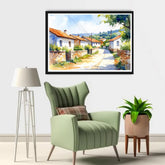 Framed painting of a village scene above a green armchair with a lamp and plant in the room.