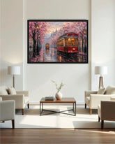 A framed canvas art print depicting a romantic Parisian street scene with red trolleys, pink cherry blossom trees, and warm glowing windows, displayed on a white wall in a modern living room setting.