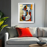 A framed abstract wall art print featuring a stylized violin design over susiheet mc, displayed above a modern gray sofa with red and green pillows in a living room setting.