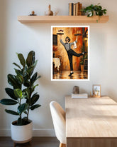 A framed art print featuring a cartoon waiter in a restaurant, displayed on a white wall above a wooden desk in a styled room with a potted plant and shelf.