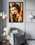 A framed wall art print depicting a woman holding a white mask, displayed in a modern living room setting above a gray velvet armchair.