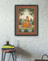 Framed artwork of a woman in an orange saree on a white brick wall with a small table and books below.