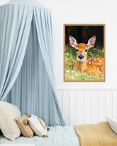 A framed art print of a cute deer in a forest meadow, styled on a white wall above a bed with a light blue canopy and neutral-toned bedding.