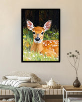 A framed vertical art print of a fawn resting in a grassy field with white flowers, displayed on a beige wall above a styled bed in a bedroom setting.